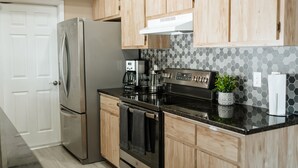 A modern kitchen with wooden cabinets, stainless steel appliances, a black countertop, and a hexagonal tile backsplash. - Cozy Home 20 min to Beach! Private Backyard. Pet Friendly (Fort Myers)