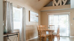 A dining area with a wooden table and chairs, a sliding barn door, and a large window with blinds. - Cozy Home 20 min to Beach! Private Backyard. Pet Friendly (Fort Myers)