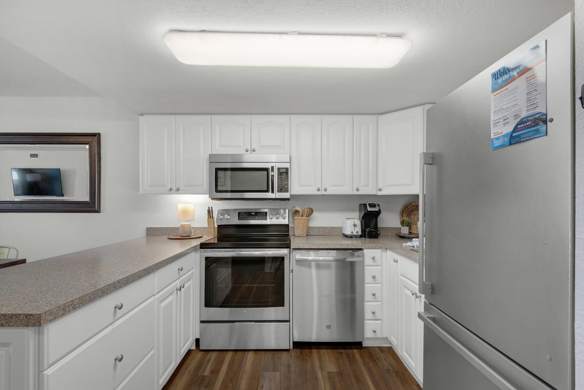 A modern kitchen with white cabinets, stainless steel appliances, and a wooden floor.
