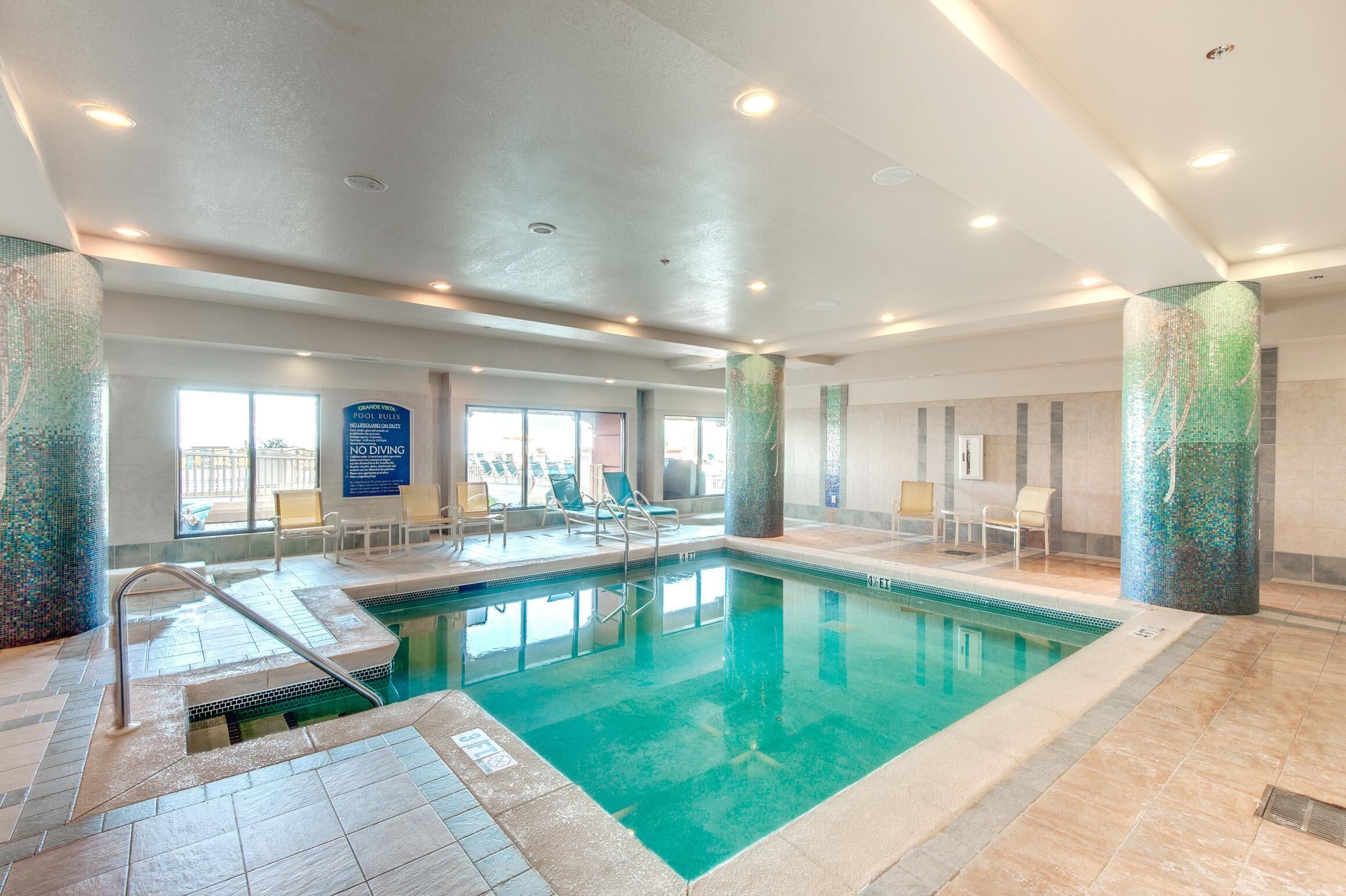 An indoor swimming pool with clear water, surrounded by lounge chairs and a tiled floor.