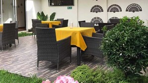 Un patio al aire libre con mobiliario de mimbre y manteles amarillos, rodeado de follaje y decoración mural.