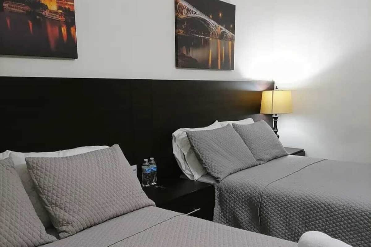 Habitación de hotel con dos camas, una mesita de noche con lámpara y dos cuadros en la pared.