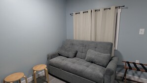 Una sala de estar pequeña y moderna con un sofá gris, dos taburetes de madera y un banco de madera.