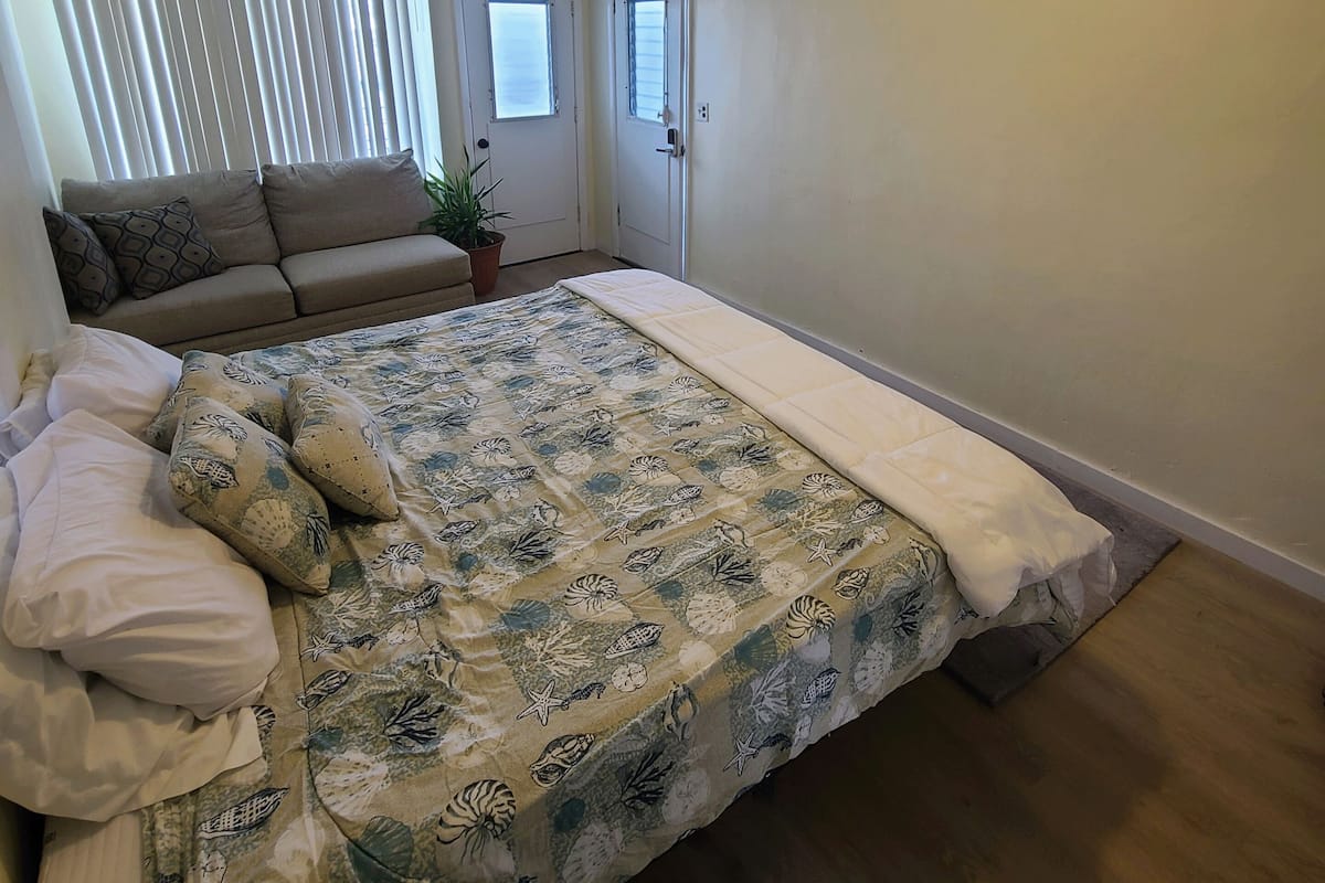 A bedroom with a large bed, a window with blinds, a door, and a ceiling light.