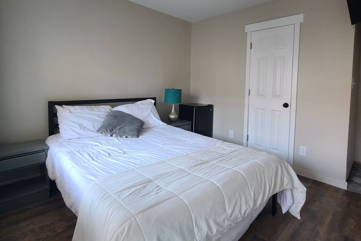 A bedroom with a bed, a nightstand, a lamp, a ceiling fan, and a door.