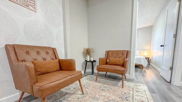 Een moderne woonkamer met twee bruine leren banken, een vloerkleed met een patroon en een klein bijzettafeltje met een kaars.
