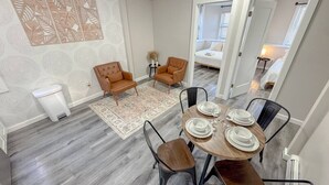 Een eetgedeelte met een ronde tafel gedekt voor vier personen, omringd door vier stoelen, een klein tapijt en een decoratief paneel aan de muur.