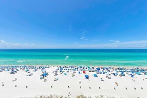 A beach with numerous umbrellas and sun loungers, a clear blue sky, and a calm sea.