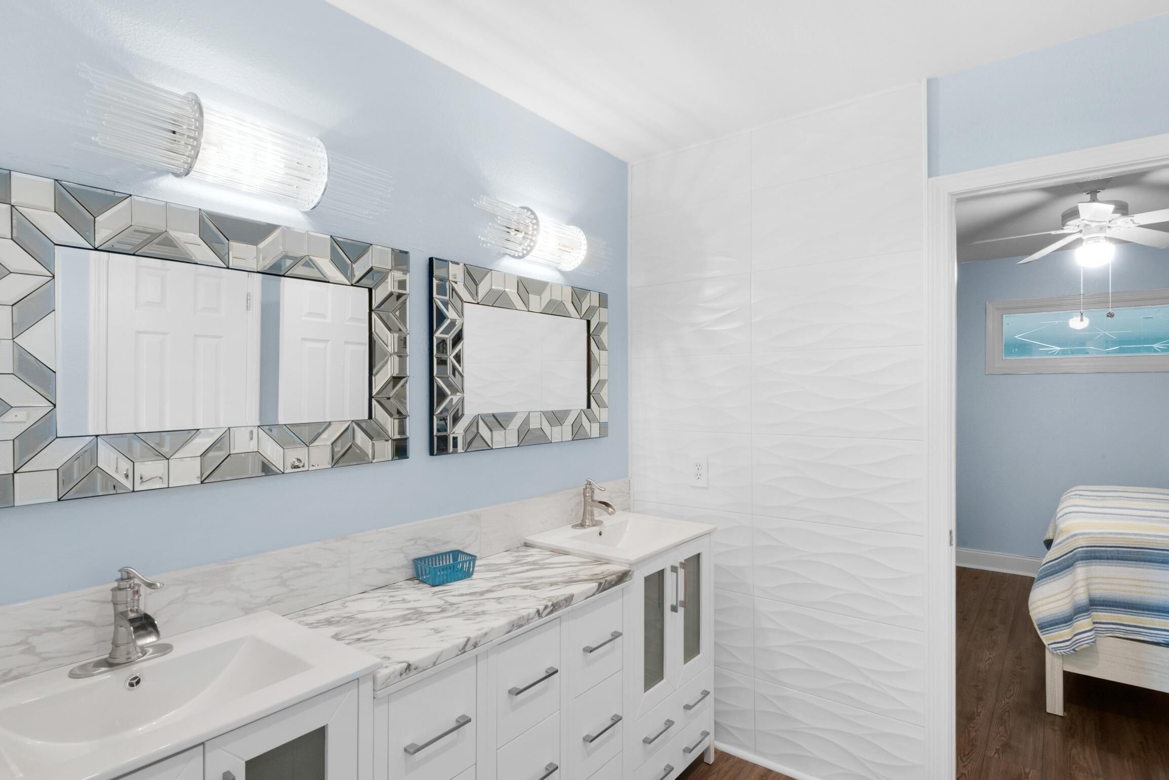 A bathroom with a white vanity, two mirrors with geometric patterns, a white sink, and a ceiling fan.
