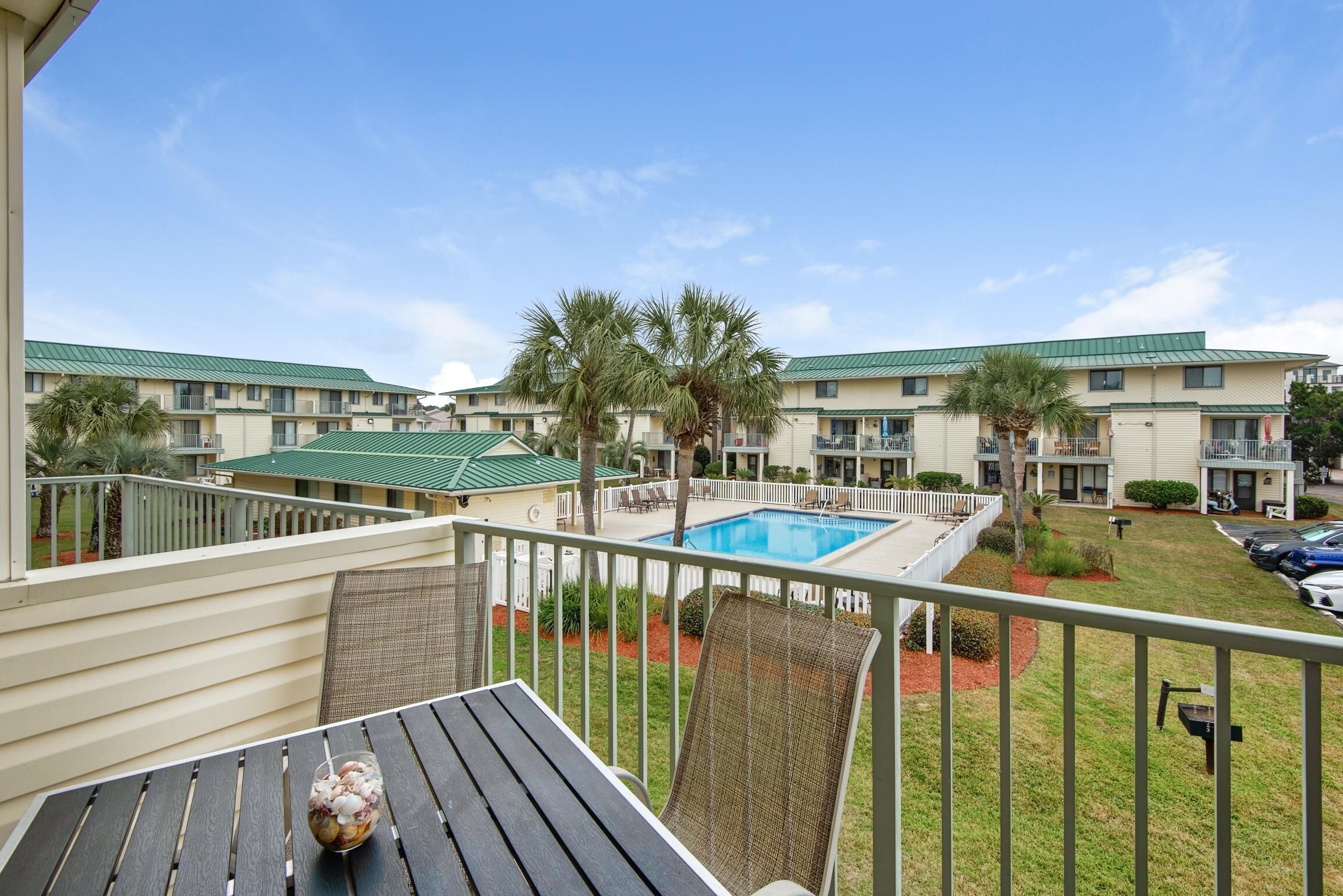 A balcony with a pool, palm trees, and a view of a hotel building.