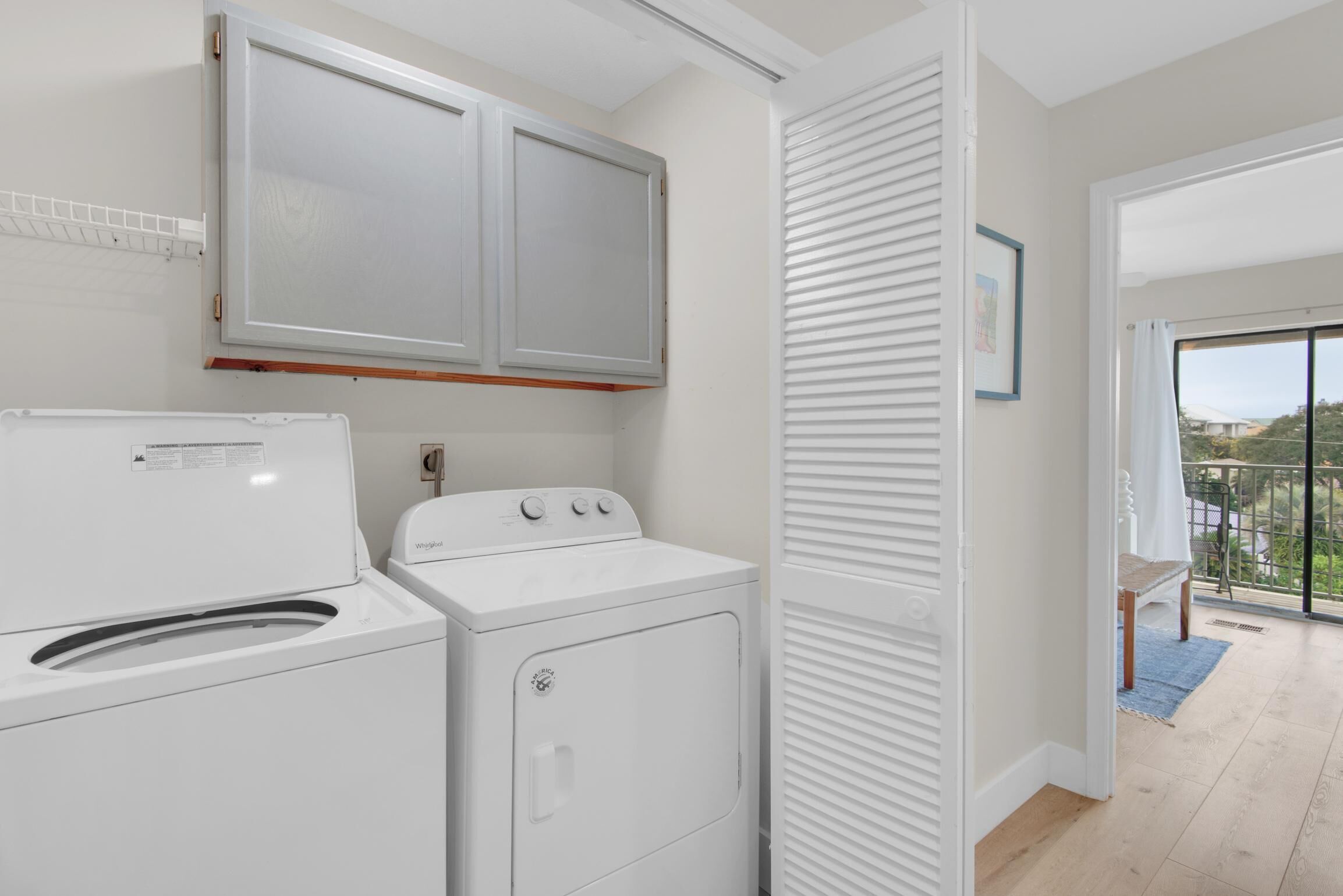 A laundry area with a front-loading washer and dryer, a white cabinet above, and a sliding door closet.