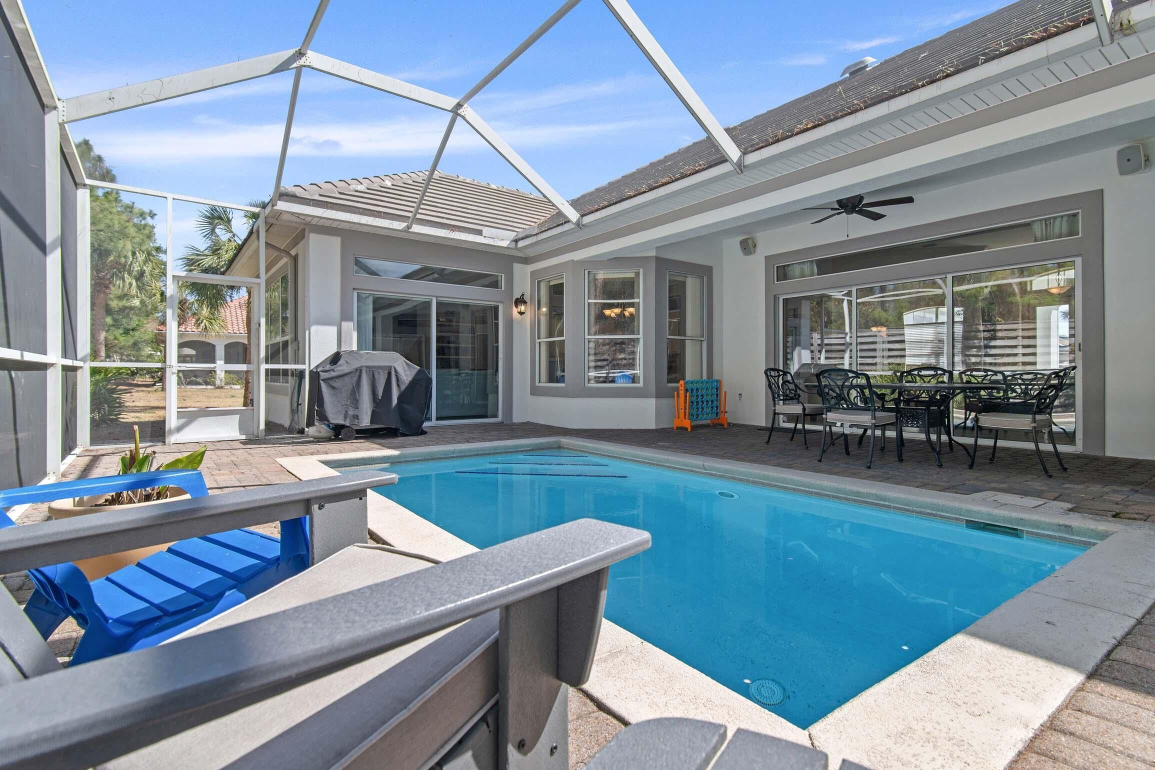 A covered outdoor swimming pool with a patio area, including a table and chairs, and a ceiling fan.