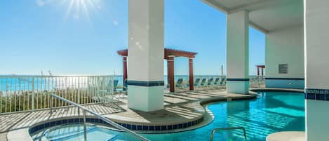 An indoor swimming pool with a view of the ocean, surrounded by white pillars and a pergola.