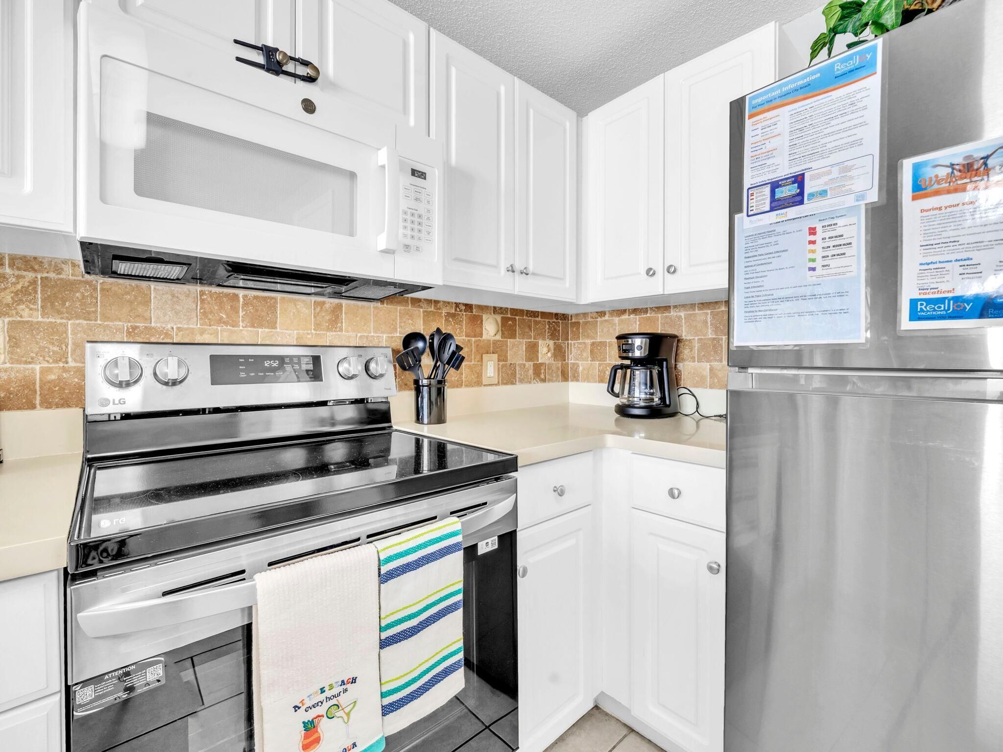 Una cucina moderna con mobili bianchi, un frigorifero in acciaio inossidabile, un forno a microonde, un forno e una macchina da caffè.