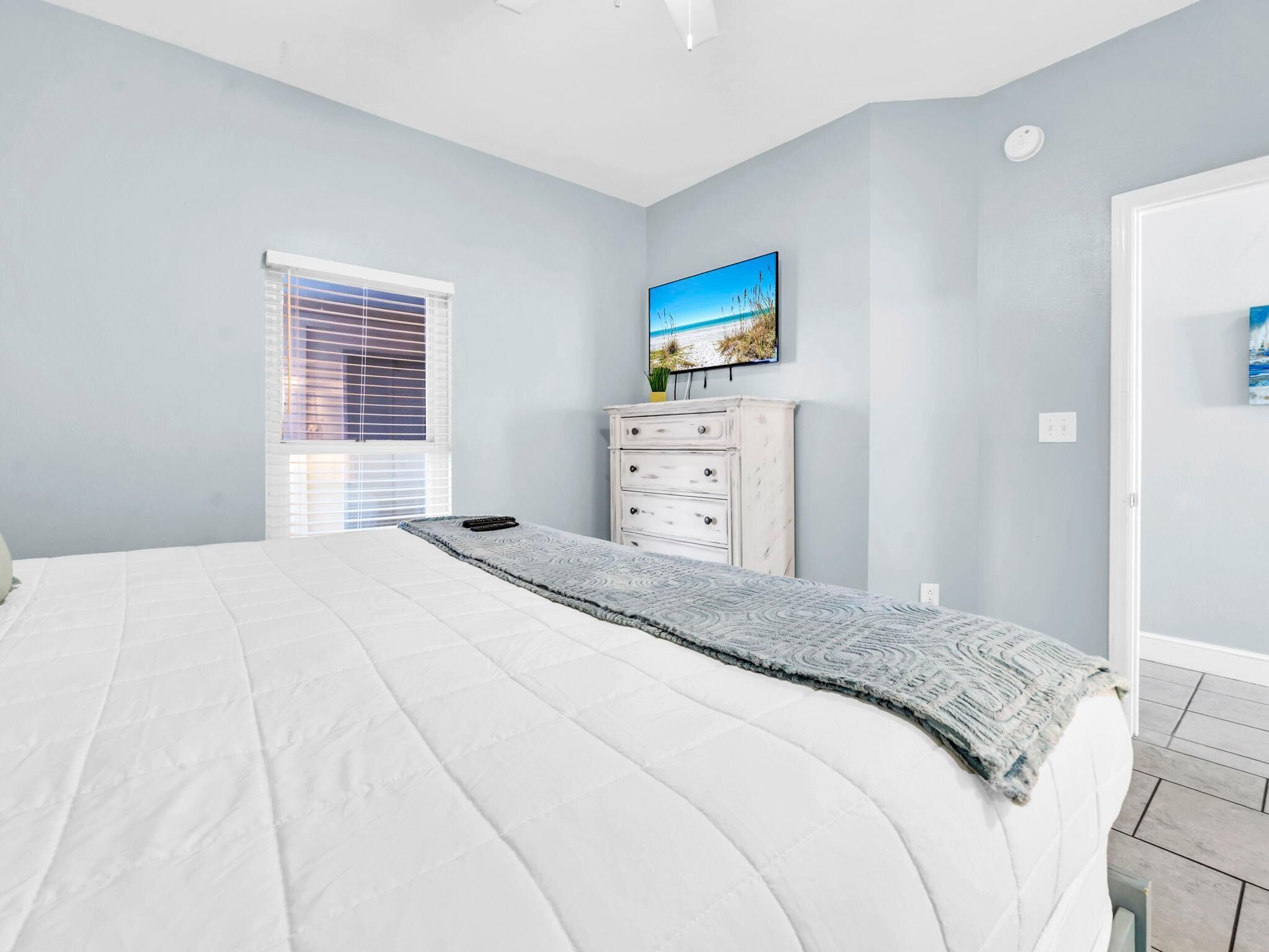 A bedroom with a bed, a dresser, a window with blinds, and a painting on the wall.