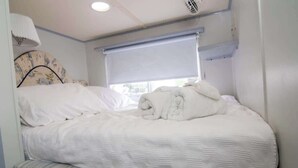 A single bed with a headboard, a window with a blind, and a ceiling light fixture. - Paradise Found: Luxury Roof Deck (Boston)