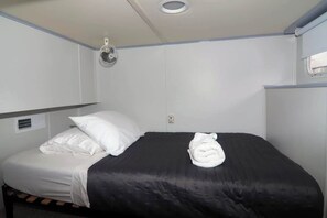 A single bed with a black mattress and white pillows, a white towel on the bed, a ceiling fan, and a window with blinds.