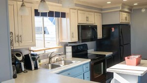 A kitchen with white cabinets, a black refrigerator, a stove, and a sink. - Paradise Found: Luxury Roof Deck (Boston)