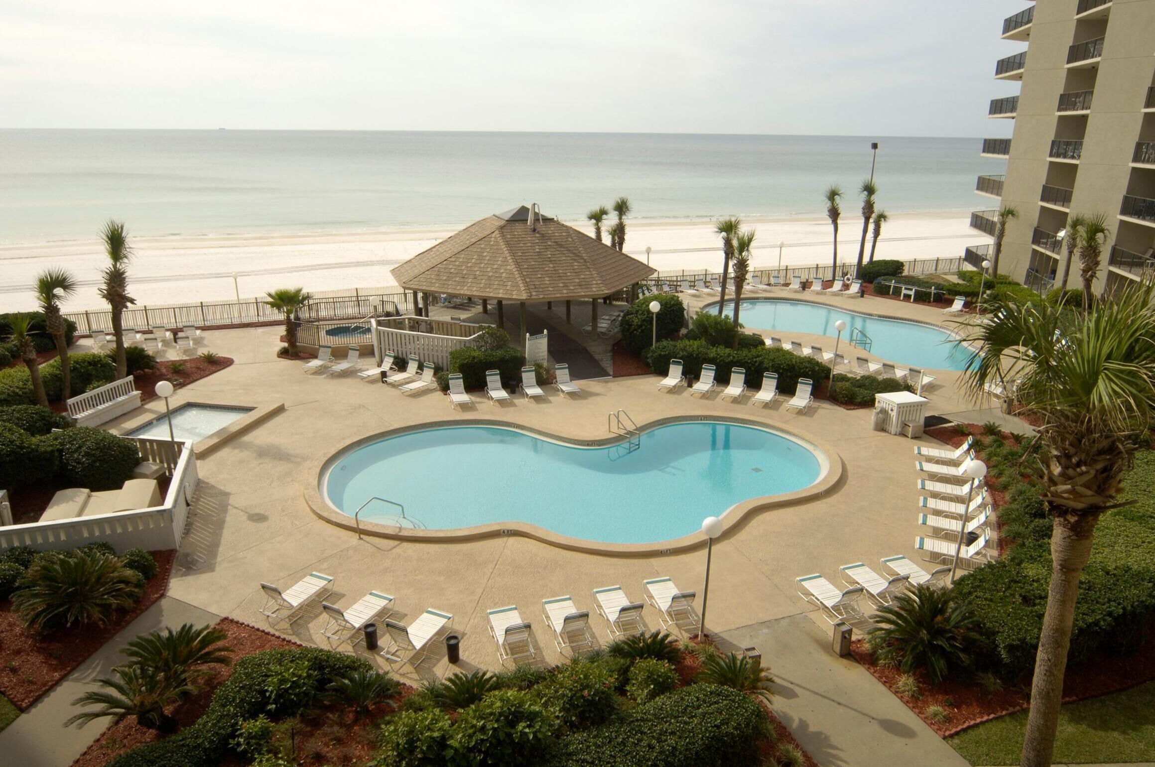 A resort pool area with two pools, lounge chairs, a gazebo, and a beach view.