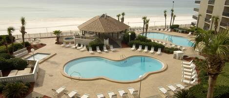 A resort pool area with two pools, lounge chairs, a gazebo, and a beach view.