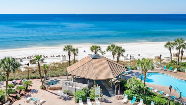 A beachside resort with a swimming pool, lounge chairs, and a gazebo overlooking the ocean.