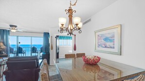 A spacious dining area with a glass table, wicker chairs, and a chandelier.