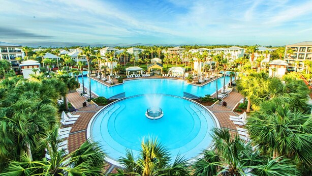 A large circular pool with a central fountain, surrounded by lounge chairs and palm trees. - Dock Holiday (Panama City Beach)