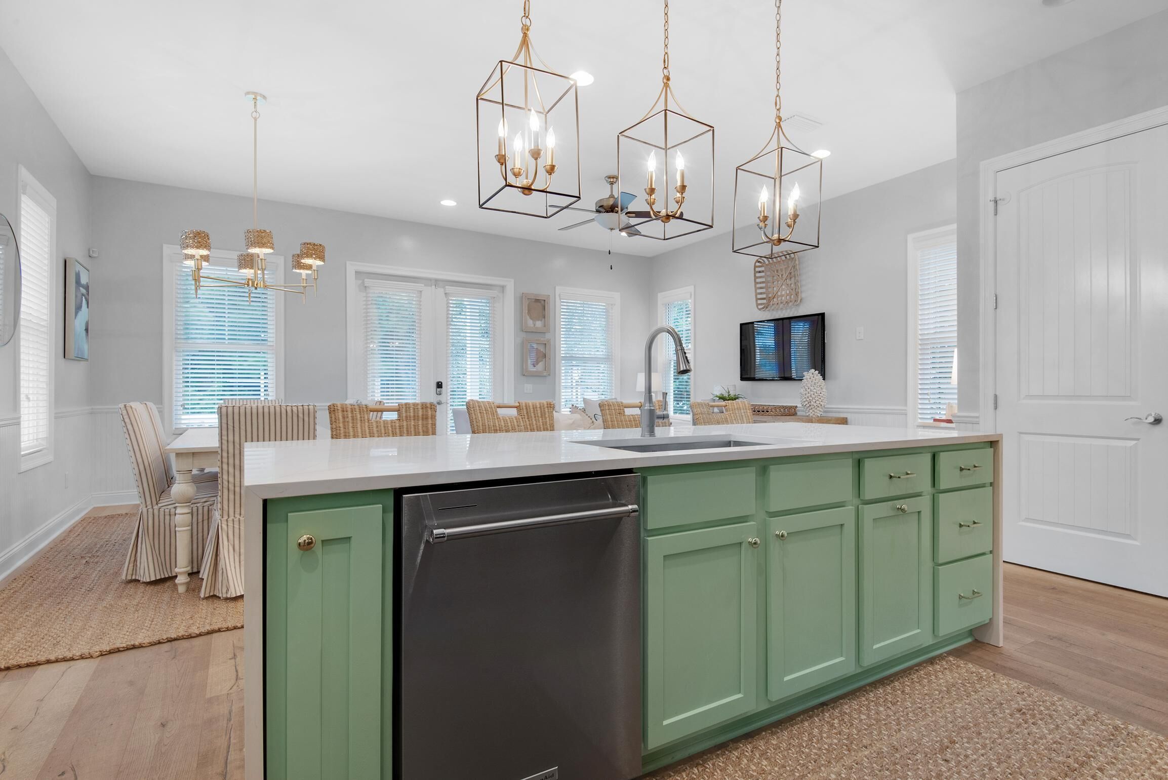 A modern kitchen with a central island, green cabinets, and pendant lighting.
