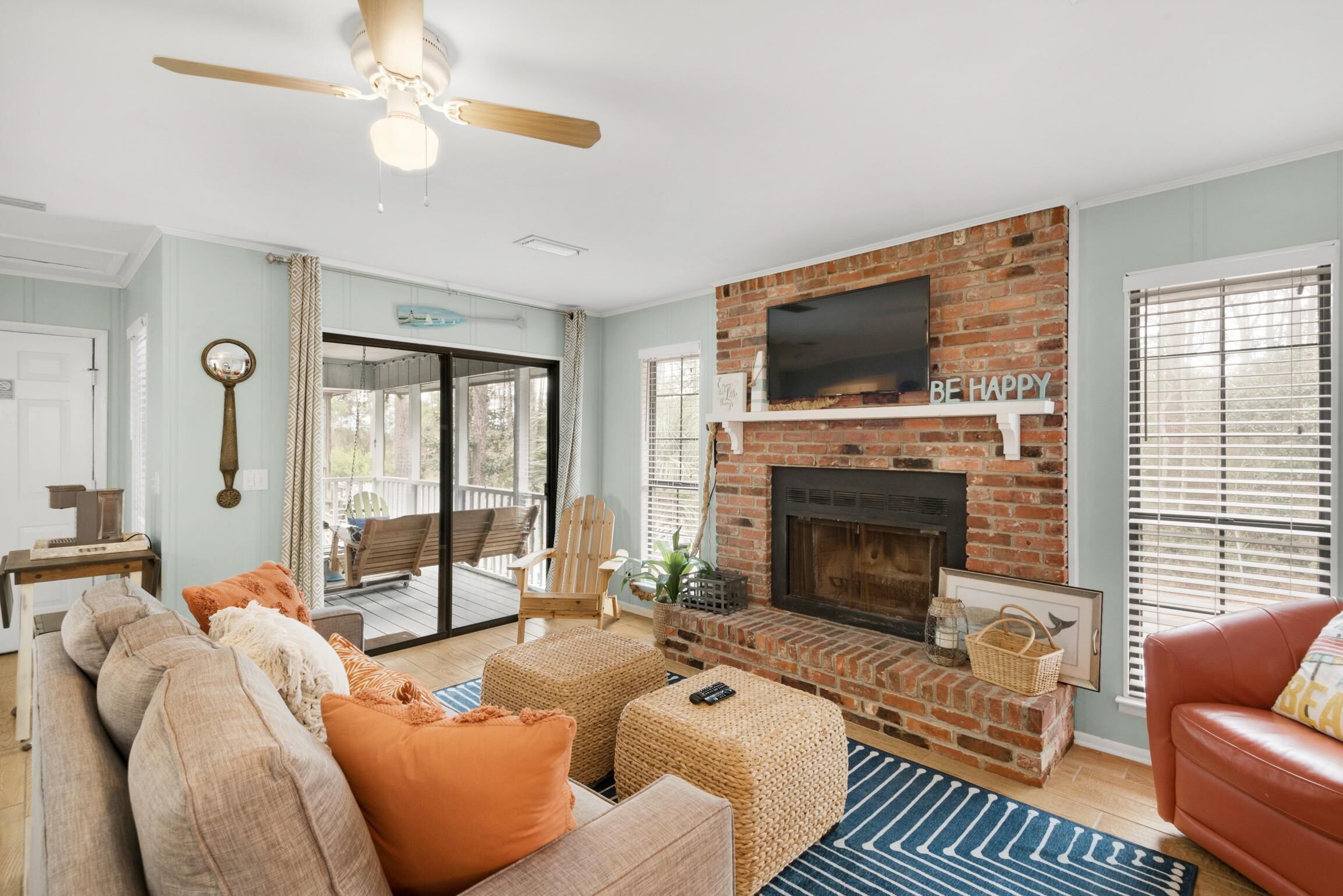 A living room with a brick fireplace, a ceiling fan, and a large window.