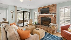 Ein Wohnzimmer mit Kamin aus Backstein, Deckenventilator und großem Fenster.