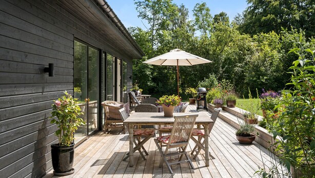 En udendørs terrasse med træterrasse, et bord med stole og en grill.