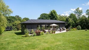Et moderne hus med en patio, udendørs møbler og en velplejet græsplæne.
