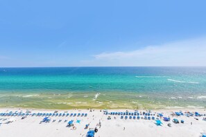 A beach with rows of blue umbrellas and sun loungers, a clear blue sea, and a sandy shore. - Majestic Beach Towers 2-1509 (Panama City Beach)