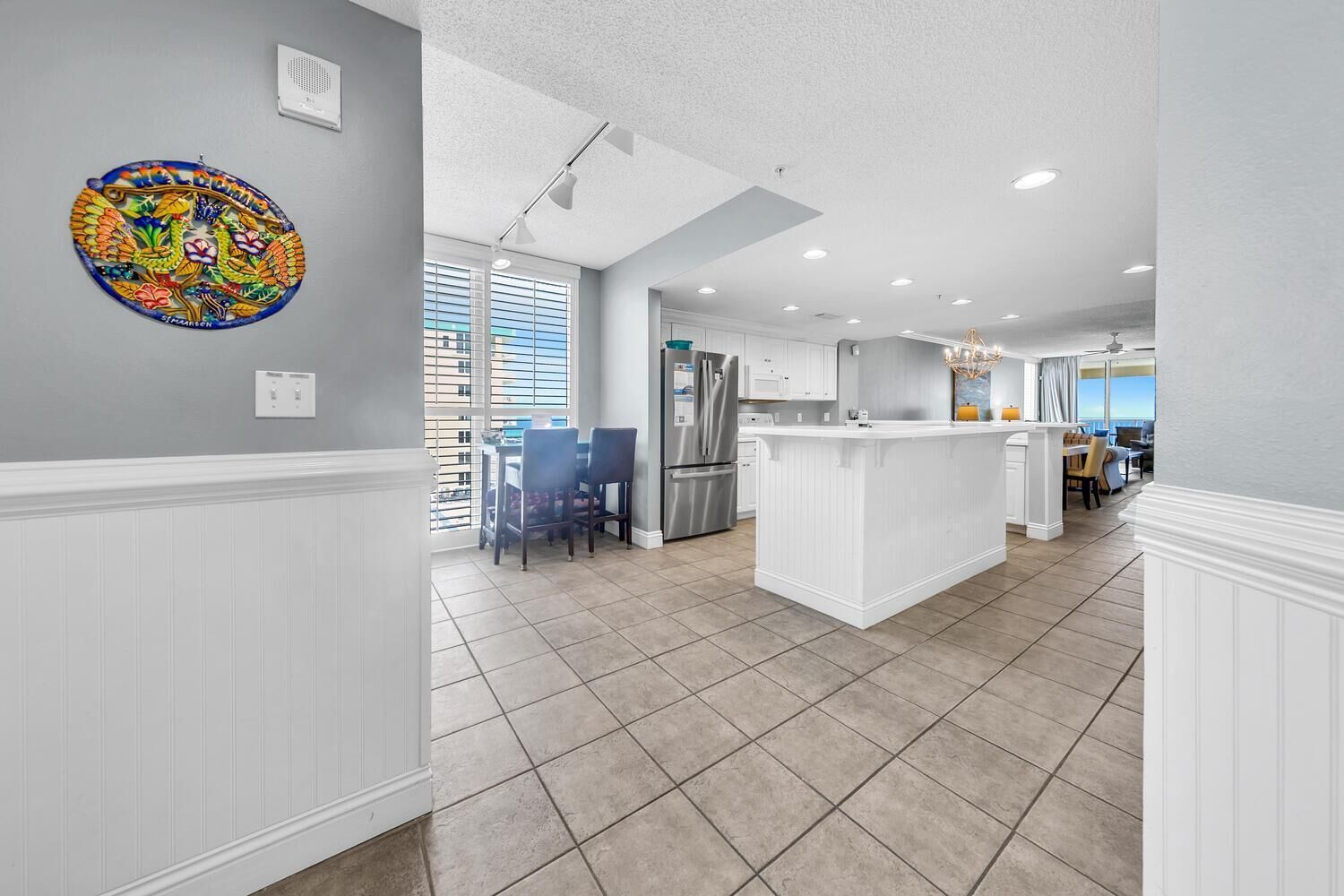 A modern kitchen with white cabinetry, a central island, and a dining area with chairs.