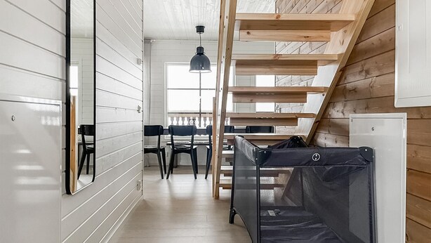 Un couloir étroit avec un escalier menant à une mezzanine, une table à manger avec des chaises et un petit espace nuit fermé.
