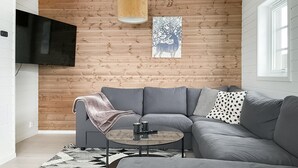 Un salon moderne avec un canapé d’angle gris, une table basse ronde et un mur en bois orné d’un tableau.