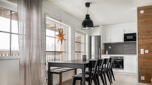 Une cuisine moderne avec des meubles blancs, une table à manger noire et des chaises. Un luminaire en forme d’étoile est suspendu au-dessus de la table.
