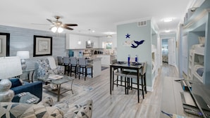 A modern living room with a sofa, coffee table, and a dining area with chairs and a table. - Horizon South 74F (Panama City Beach)