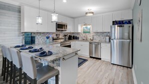 A modern kitchen with white cabinets, a granite countertop, stainless steel appliances, and pendant lighting. - Horizon South 74F (Panama City Beach)