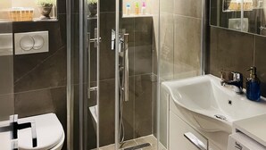 Un baño moderno con cabina de ducha de vidrio, lavabo blanco y inodoro.