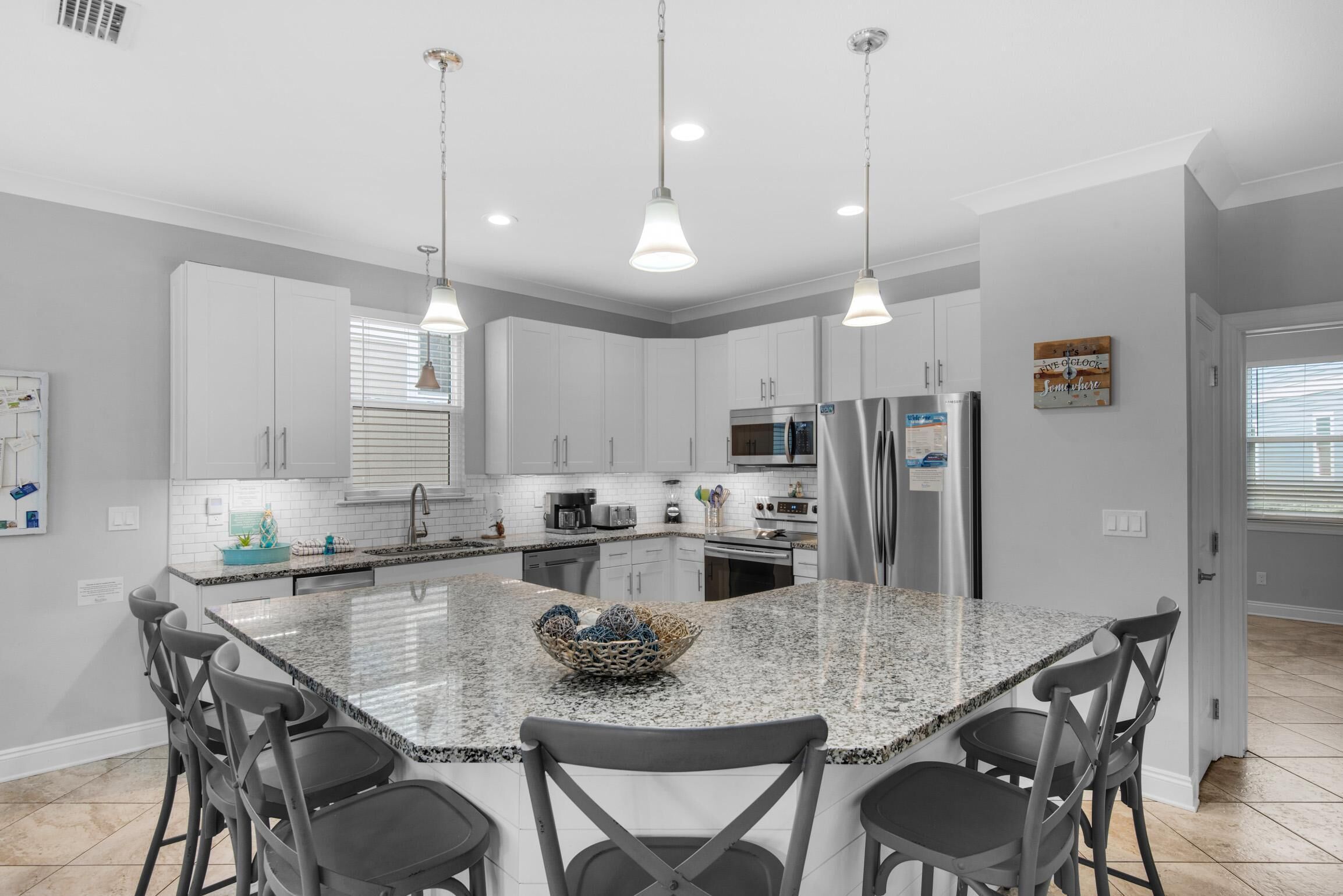 A modern kitchen with white cabinets, a granite island, and bar stools.
