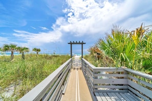 A wooden boardwalk leading to a beach with a pergola structure.