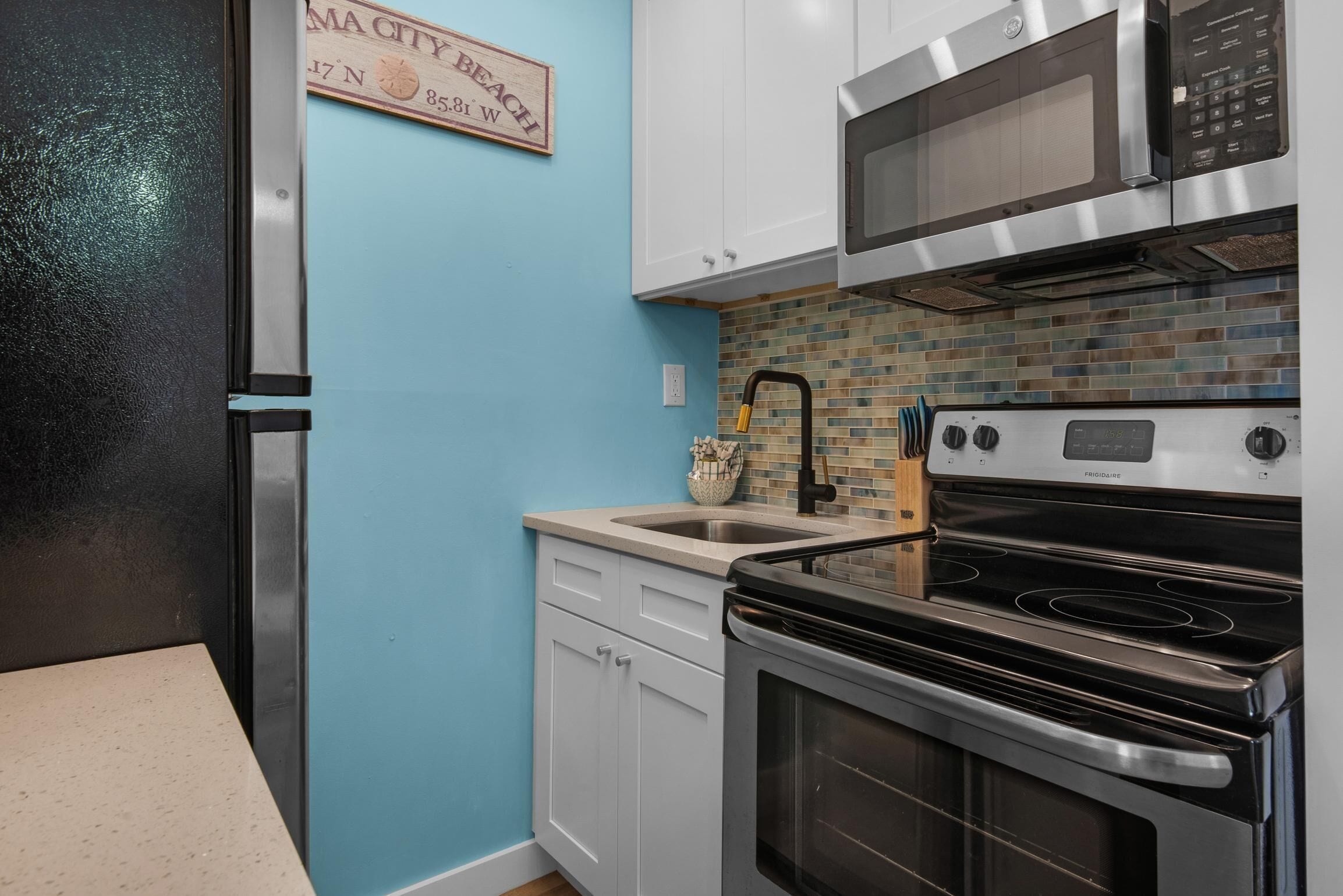 Una cocina con gabinetes blancos, un refrigerador de acero inoxidable, un microondas, una estufa y un salpicadero de azulejos.