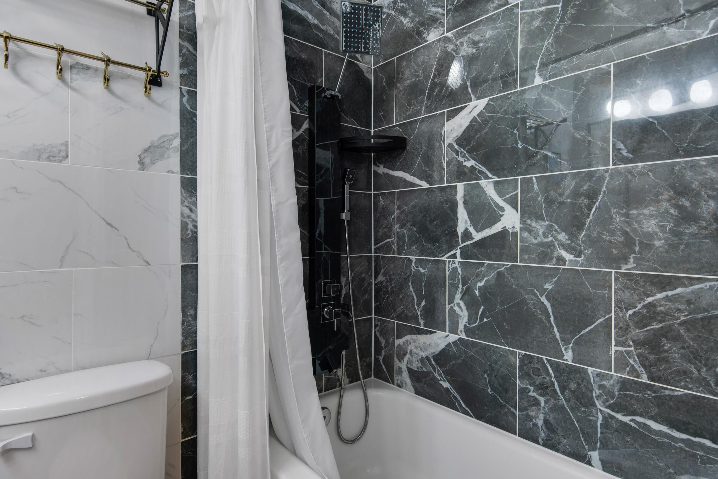 A bathroom with a toilet, a shower, and a bathtub. The walls are tiled with a marble pattern.