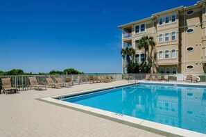 Una piscina con sillones de descanso, una cerca blanca y un edificio con varios balcones.