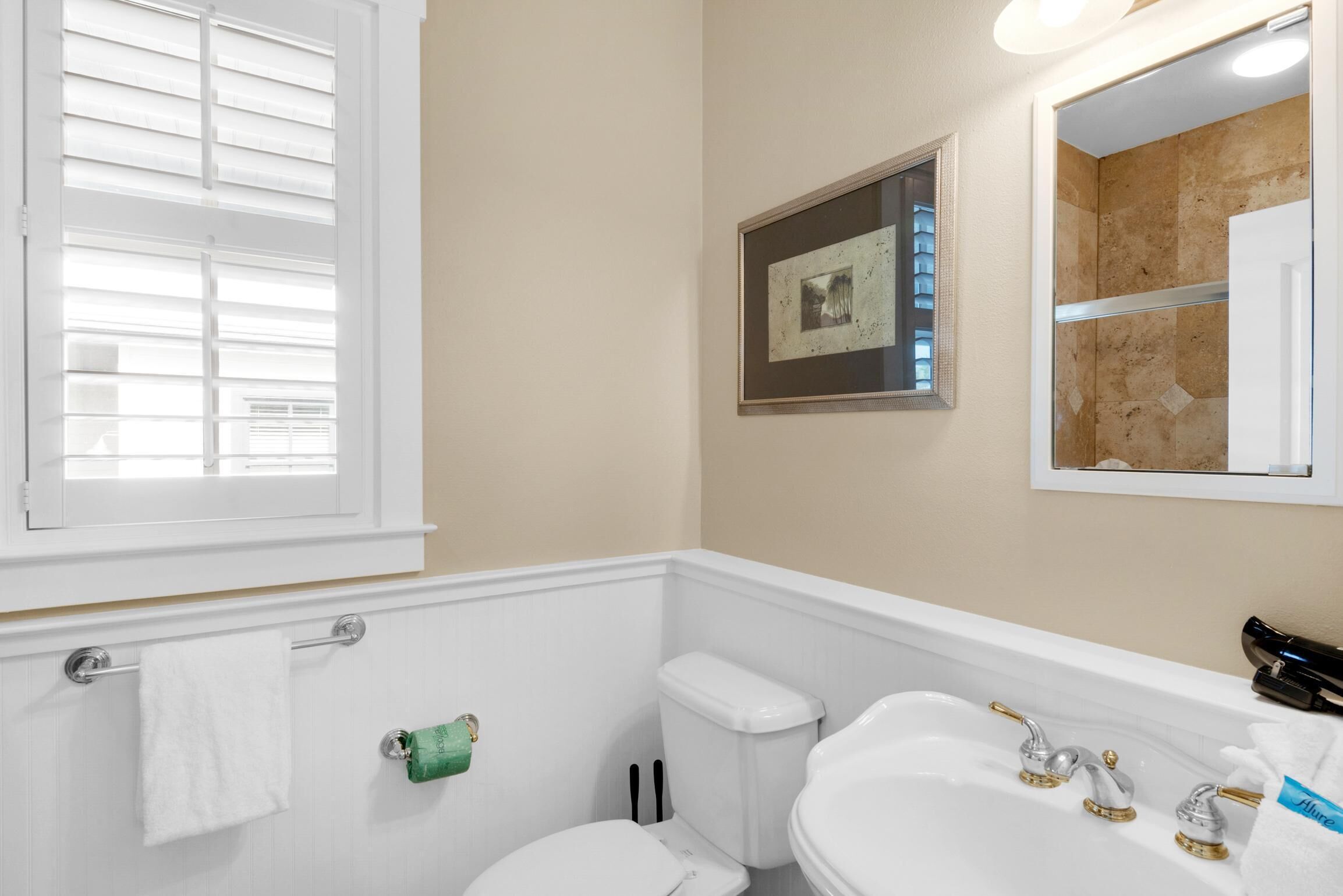 A bathroom with a toilet, sink, and window with blinds.