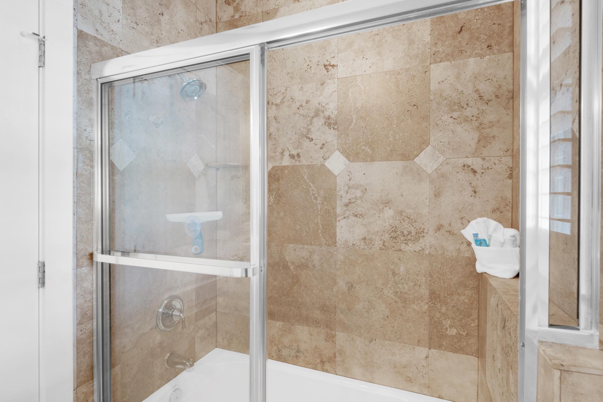 Una ducha con puerta de vidrio, azulejos color beige y una toalla blanca en la pared.