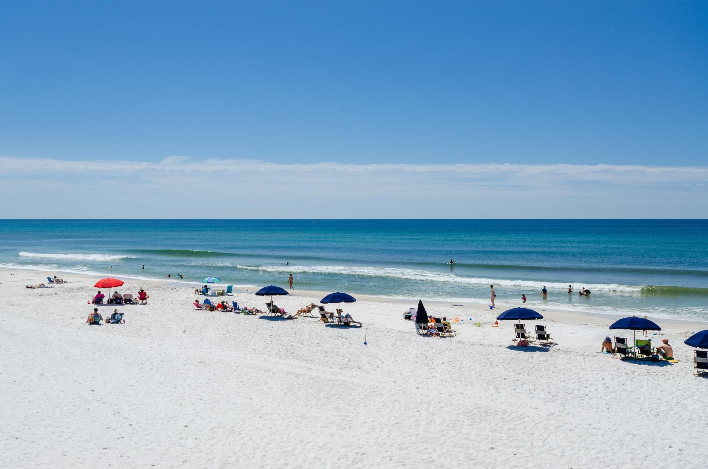 A beach with white sand, clear blue water, and people relaxing under umbrellas.