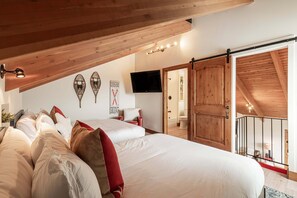 A bedroom with a large bed, two smaller beds, wooden ceiling beams, a TV, and a sliding door.