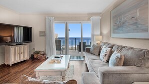 A living room with a TV, sofa, and a view of the sea. - Emerald Isle 708 (Fort Walton Beach)